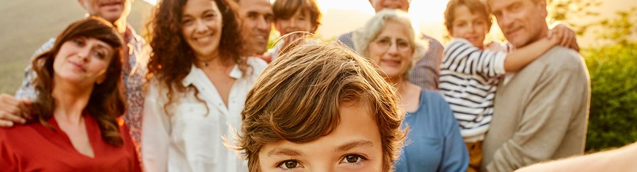 Ein Kind steht im Vordergrund und hält die Kamera für ein Selfie mit der Familie im Hintergrund