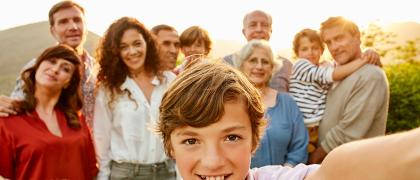 Ein Kind steht im Vordergrund und hält die Kamera für ein Selfie mit der Familie im Hintergrund